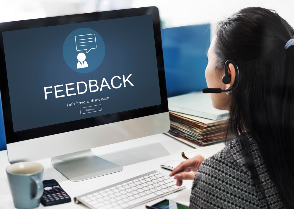 A woman with a headset engages in online feedback discussions on her computer, reflecting a professional work environment.