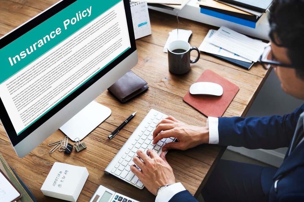 A businessman in a suit types on a keyboard, focused on an insurance policy document displayed on his computer screen.