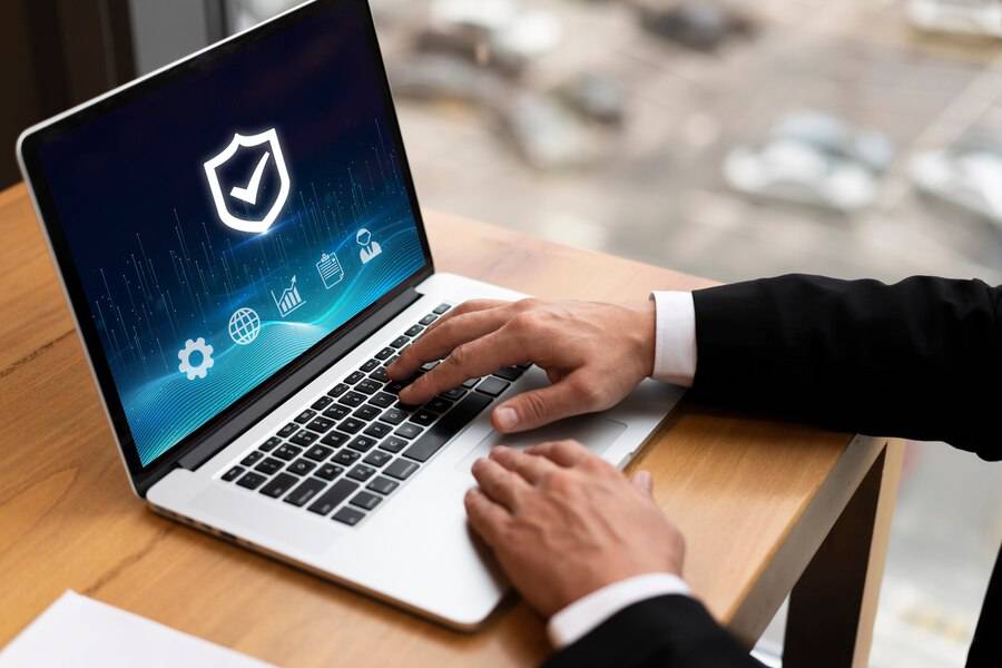 A business professional in a suit uses a laptop displaying cybersecurity icons, symbolizing digital protection and data security.