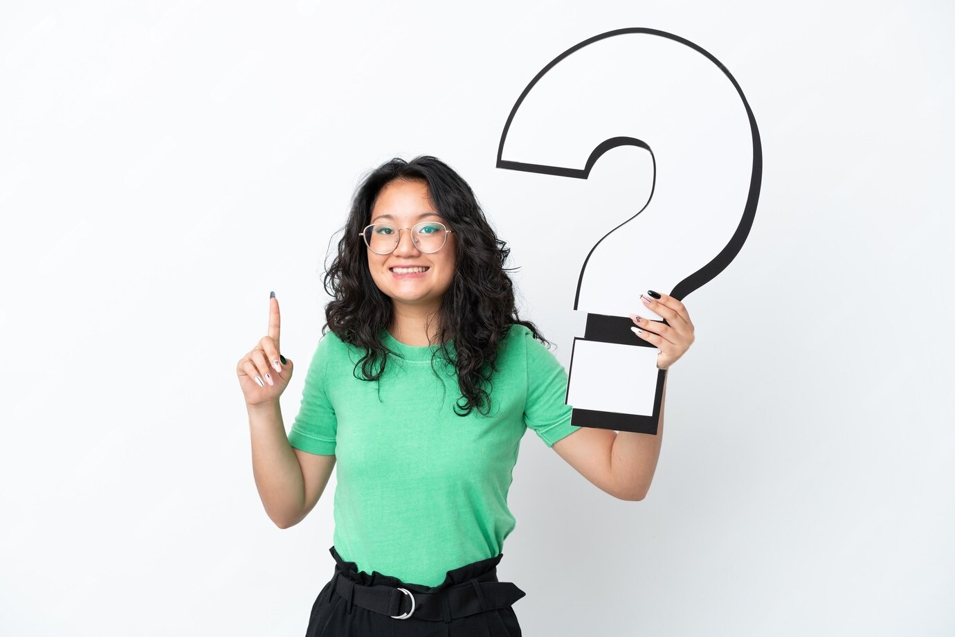 A woman in a green shirt is holding a large question mark sign and raising her index finger, suggesting curiosity or inquiry.