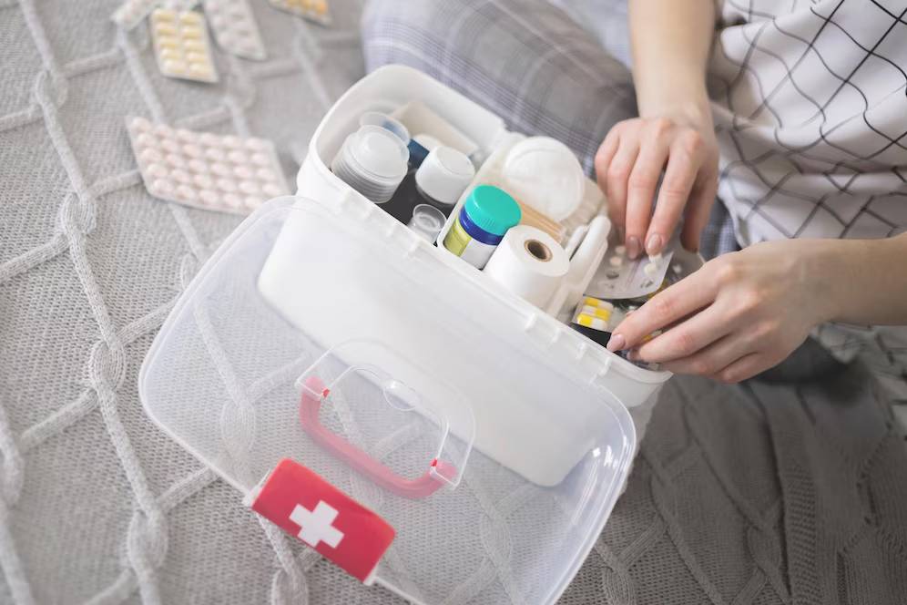 A close-up of a person organizing a first aid kit filled with various medications and supplies on a cozy, textured blanket.
