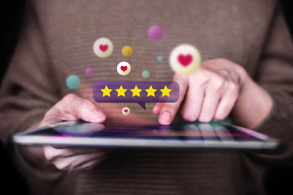 A person using a tablet with a floating five-star rating and heart icons, symbolizing online reviews and ratings.