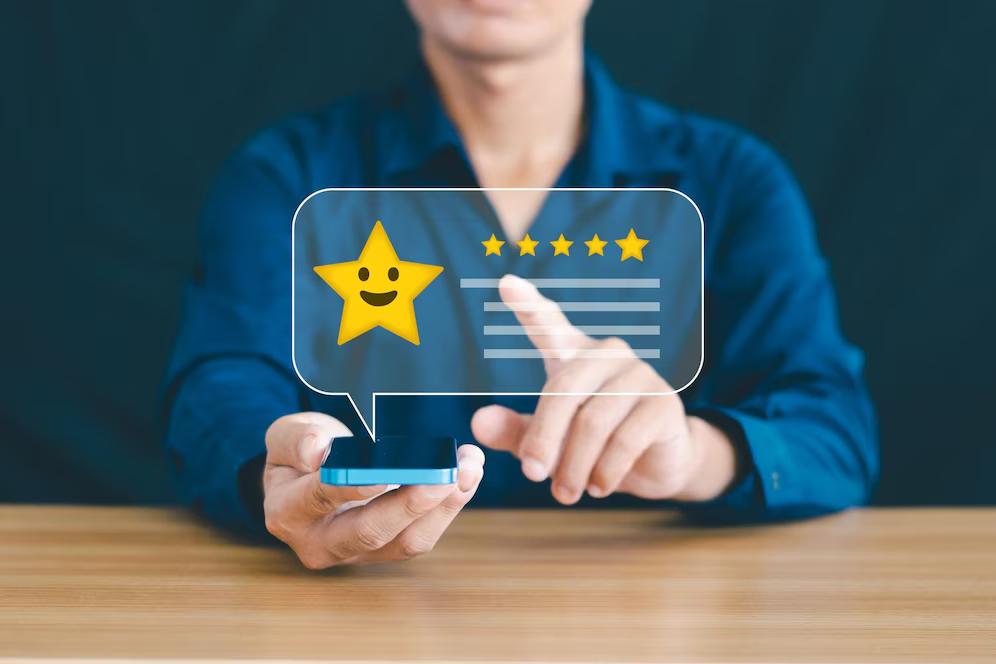 A person in a blue shirt holds a smartphone, interacting with a digital review featuring a smiling star and five rating stars.